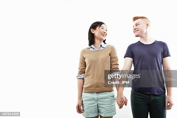studio shot of smiling young couple holding hands - portrait woman men looking at each other stock-fotos und bilder
