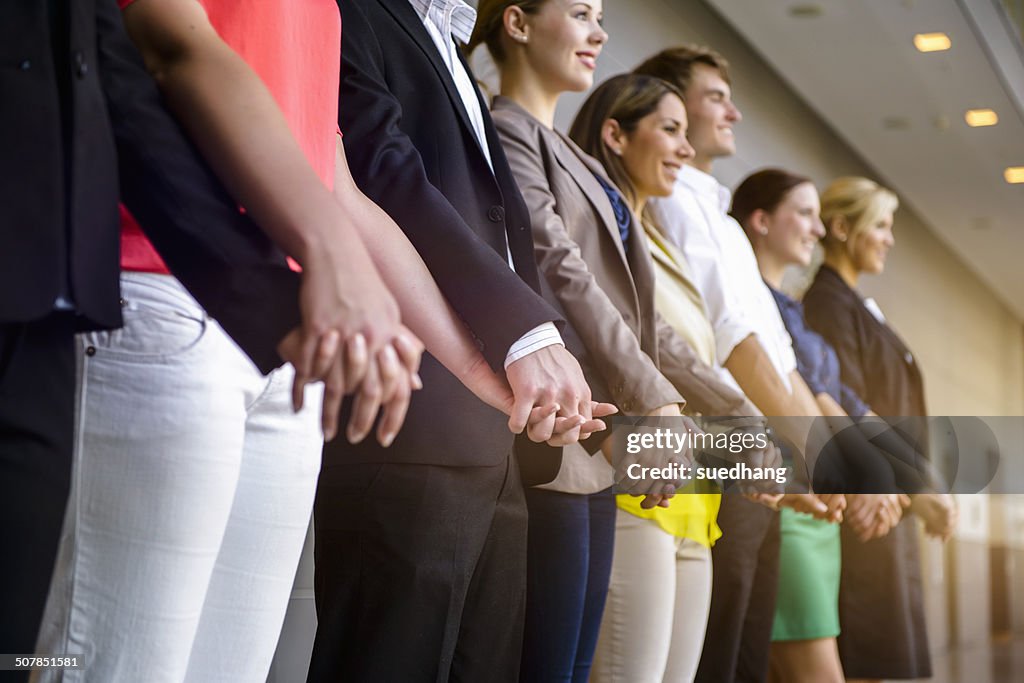 Row of businesswomen and men holding hands in office
