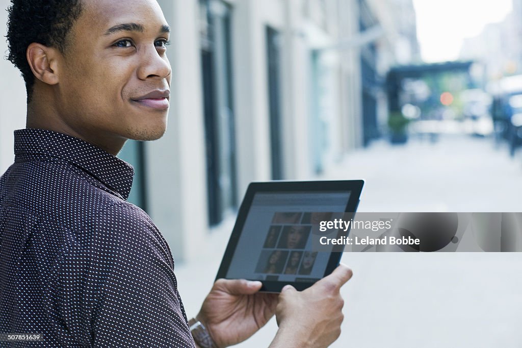 Young man on city street using digital tablet and looking over shoulder