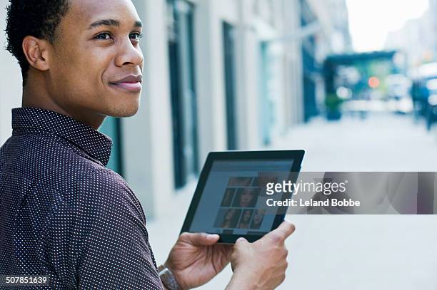 young man on city street using digital tablet and looking over shoulder - over the shoulder view stock pictures, royalty-free photos & images