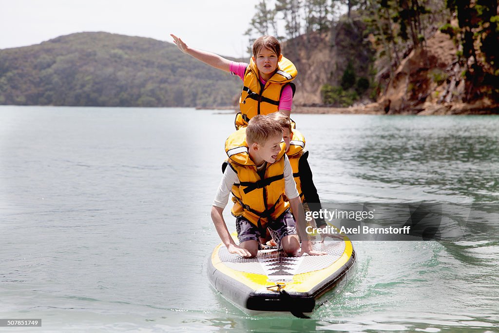 Brothers and sister standing and kneeling on paddleboard at sea