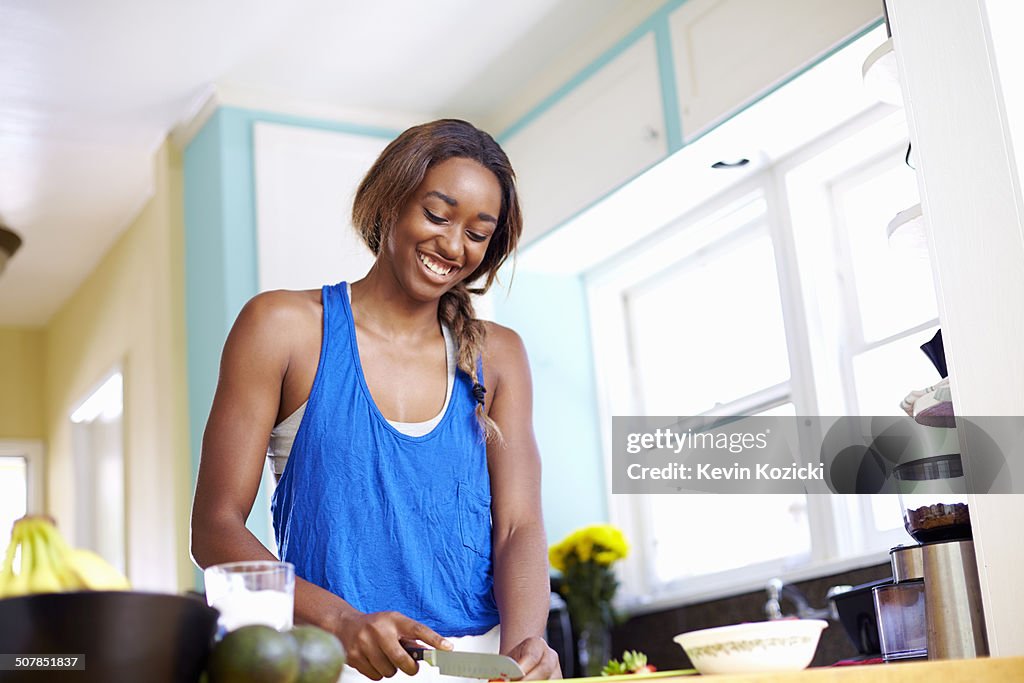 Young woman taking a training break, preparing food in kitchen