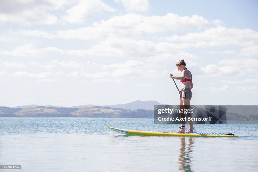 Mid adult woman stand up paddleboarding at sea