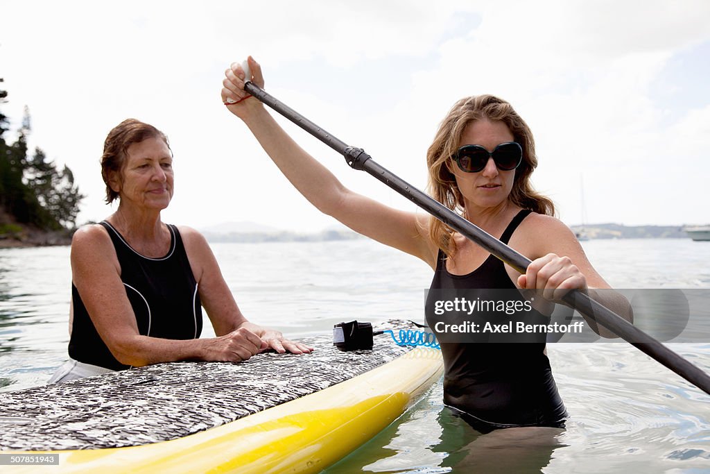 Senior woman and daughter wading with paddleboard at sea