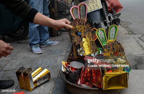 Man places votive papers, including Kitchen Gods hats and shoes, out into the street to burn as an offering in downtown Hanoi on February 1, 2016 as...