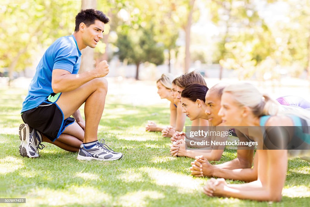 Fitness Instructor Motivating People In Doing Exercise At Park