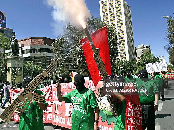 Protester, part of a group of activists wearing balaclavas, fires a rocket through a mock AKM rifle during a MayDay march in downtown La Paz,...