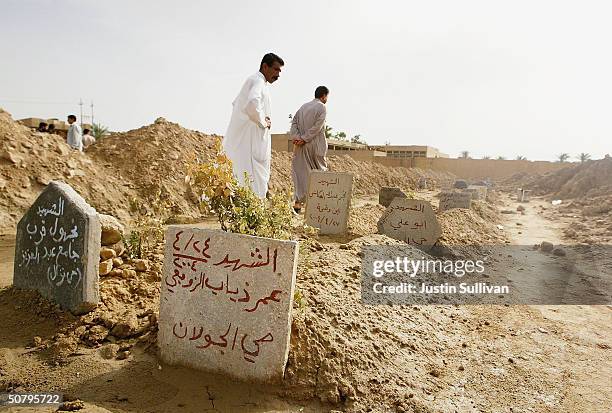 Two men look at rows of graves at an overflowing cemetery built in a soccer arena, on May 3, 2004 in Fallujah, Iraq. An estimated 1,300 Iraqis have...