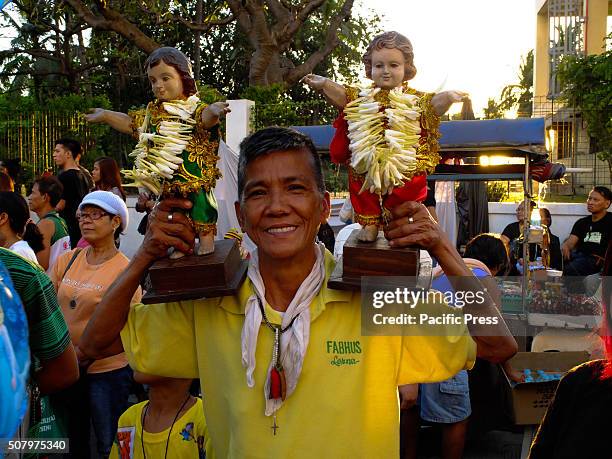 Middle-aged man proudly carries his two Sto. Niños on his shoulders while watching the parade. Catholic devotees all over the country celebrates...