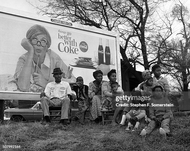 An African American family watch the march with a "Things Go Better With Coke" billboard sign in the background on Route 80, Jefferson Davis Highway...