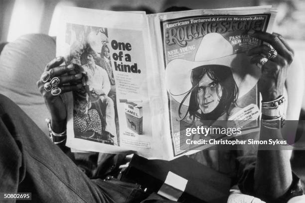 Percussionist Ollie Brown relaxes on the plane with a copy of Rolling Stone magazine during the Rolling Stones Tour of the Americas, 1975.