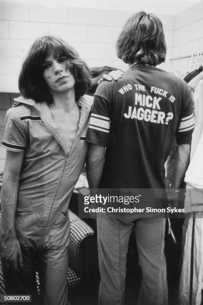 Mick Jagger leans on his stylist Pierre Laroche during the Rolling Stones Tour of the Americas, 1975. Laroche wears a t-shirt with the slogan 'Who...