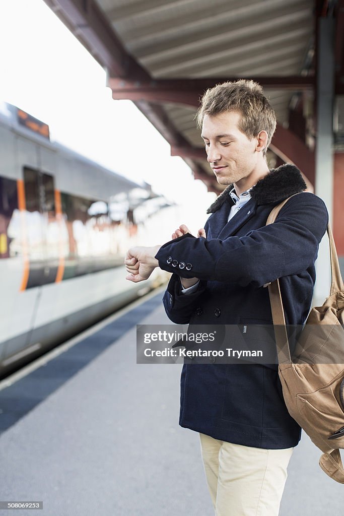 Young businessman looking at watch on railroad station