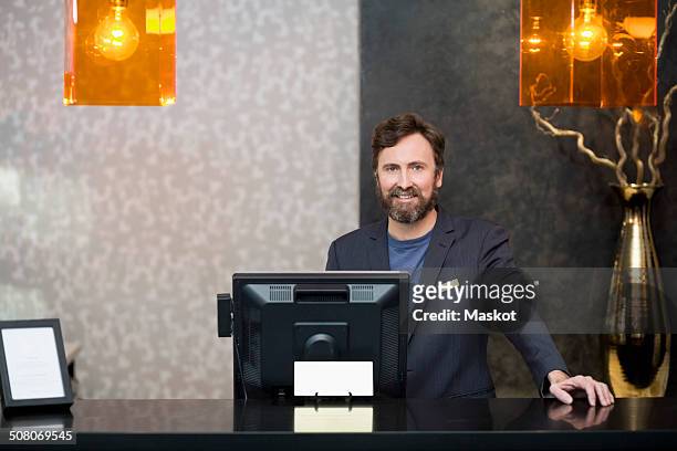 portrait of confident male receptionist standing at counter in hotel - hotel concierge stock pictures, royalty-free photos & images
