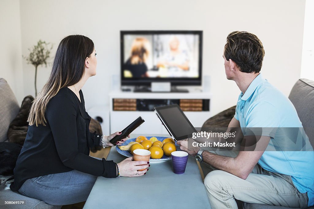 Side view of couple watching TV while having coffee at home