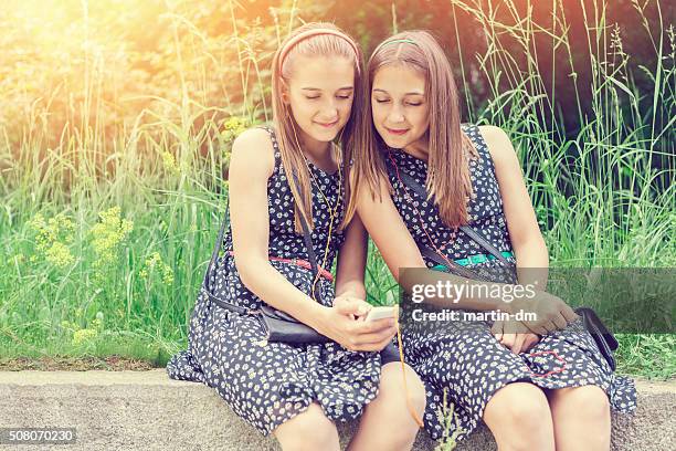 sisters texting on smartphone among nature - twin girls bildbanksfoton och bilder