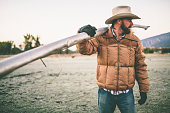 Man standing in field carries irrigation pipe over shoulder