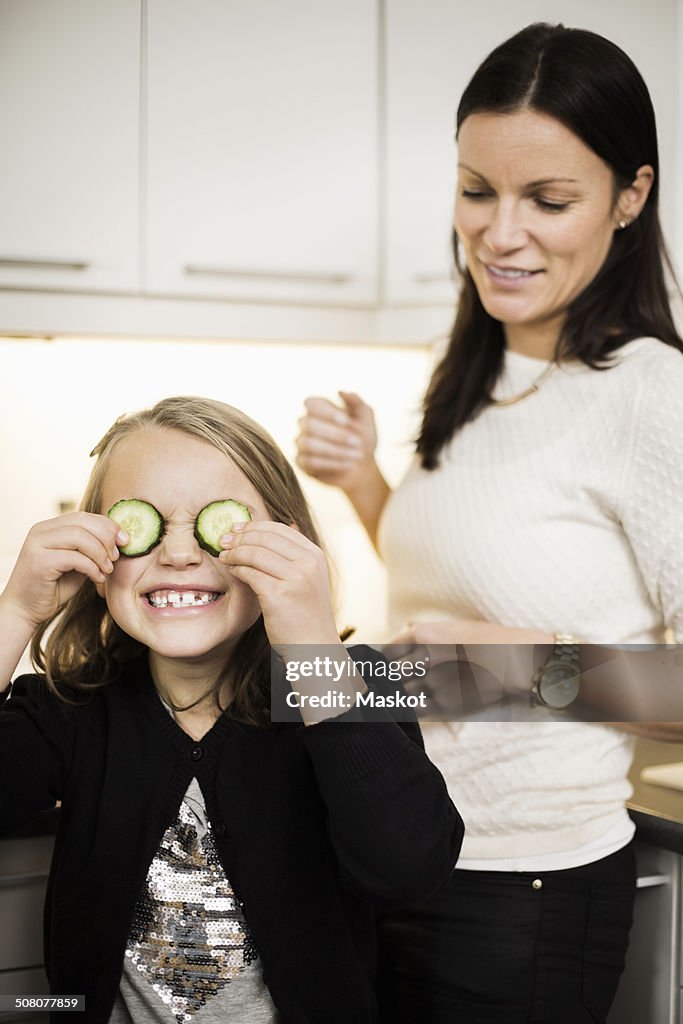 Mother looking at daughter covering eyes with cucumber slices