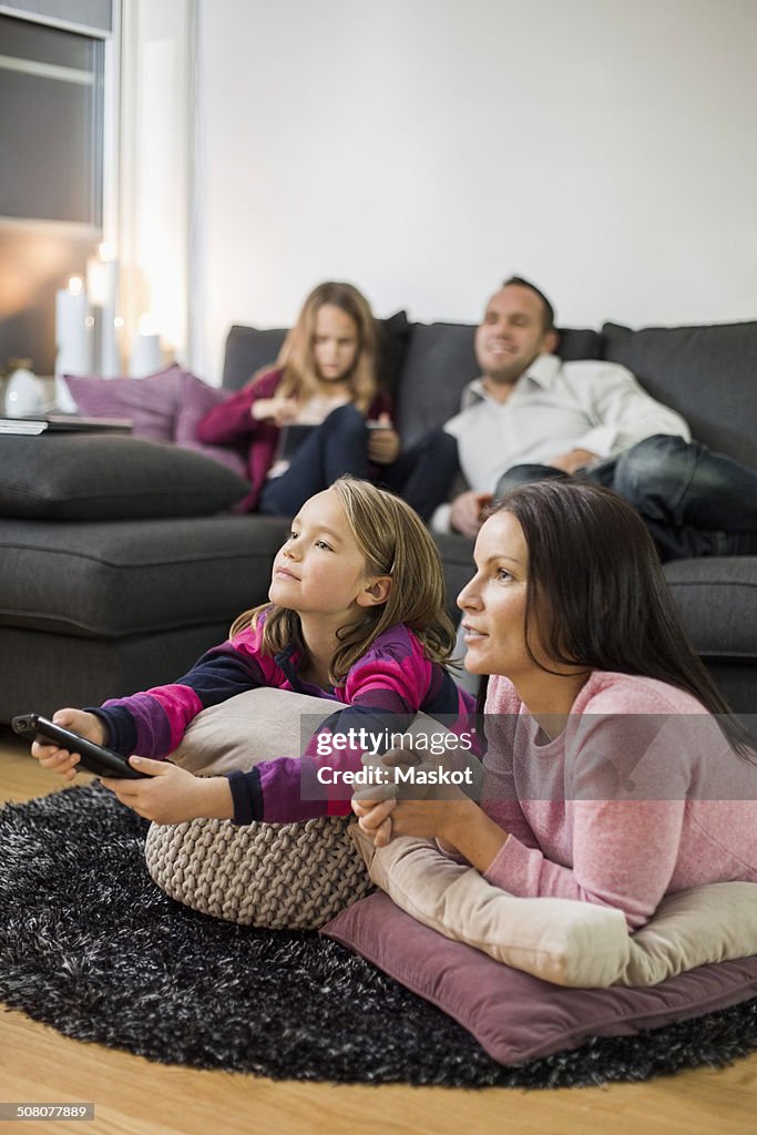 Mother and daughter watching TV on floor with family in background