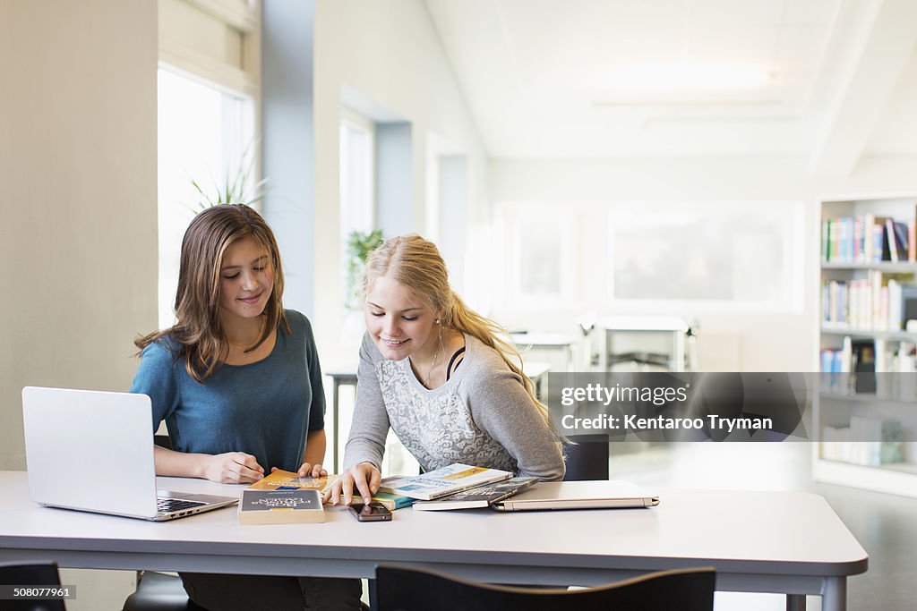 Teenage girls using mobile phone at table in school library