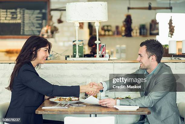 side view of businessman and businesswoman shaking hands at restaurant table - meal deal stock pictures, royalty-free photos & images