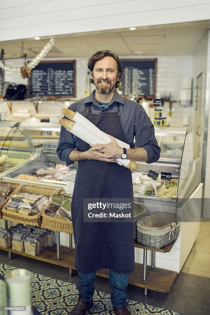 Portrait of mature male baker holding loaves of bread in supermarket