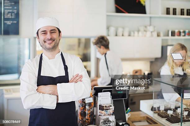 portrait of confident owner standing arms crossed in cafe - fábrica de chocolate fotografías e imágenes de stock