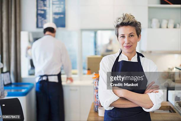 portrait of confident female owner standing arms crossed in cafe - apron stockfoto's en -beelden