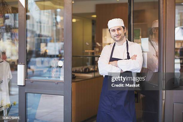 portrait of confident owner standing with arms crossed at cafe entrance - chocolate factory stock-fotos und bilder