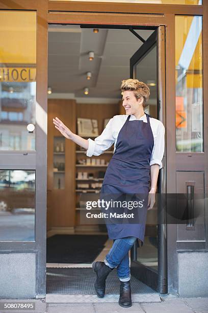 full length of happy female owner gesturing while standing at cafe entrance - bakery apron stock pictures, royalty-free photos & images