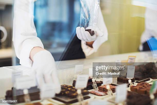 midsection of female worker packing sweet food at display cabinet in cafe - chocolate pack stock-fotos und bilder