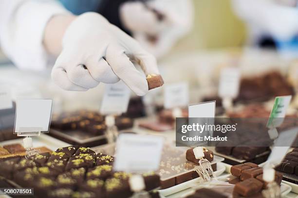 cropped image of worker holding sweet food at display cabinet at cafe - chocolate factory stock-fotos und bilder
