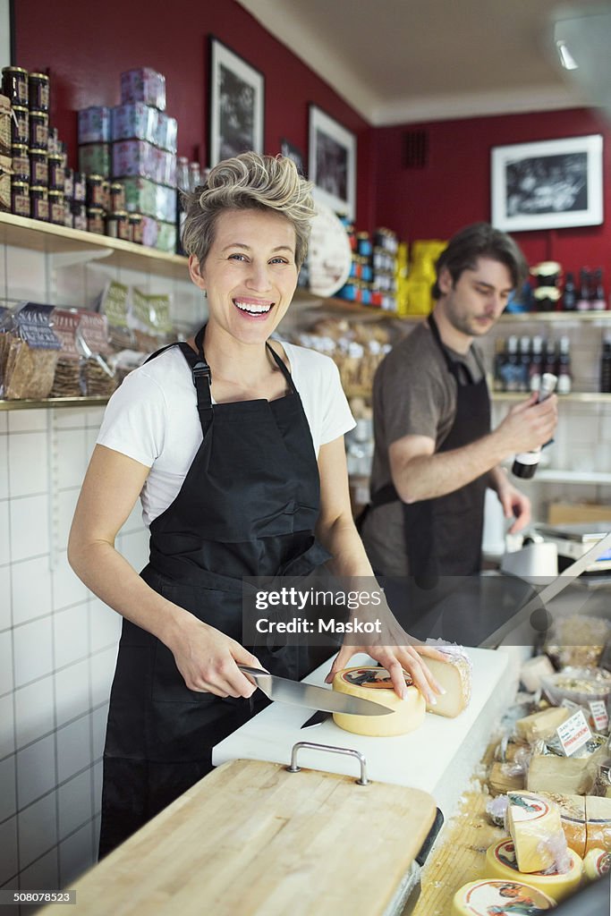 Portrait of happy saleswoman cutting cheese at counter in supermarket