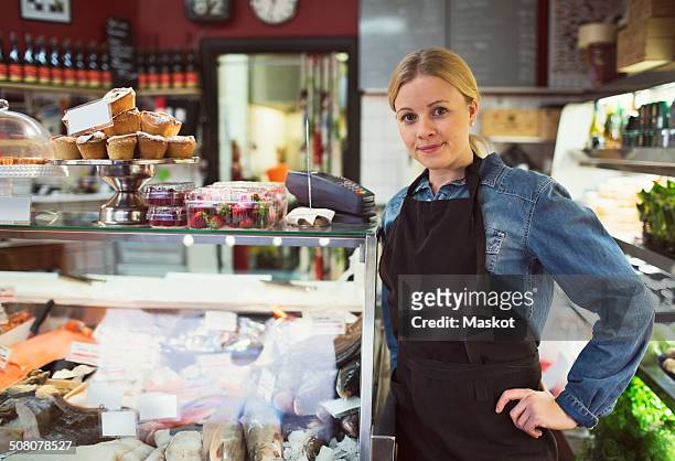 portrait of confident saleswoman standing by display cabinet in supermarket - deli bildbanksfoton och bilder