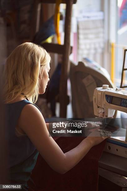 side view of female fashion designer sewing in studio - stoffeerder stockfoto's en -beelden
