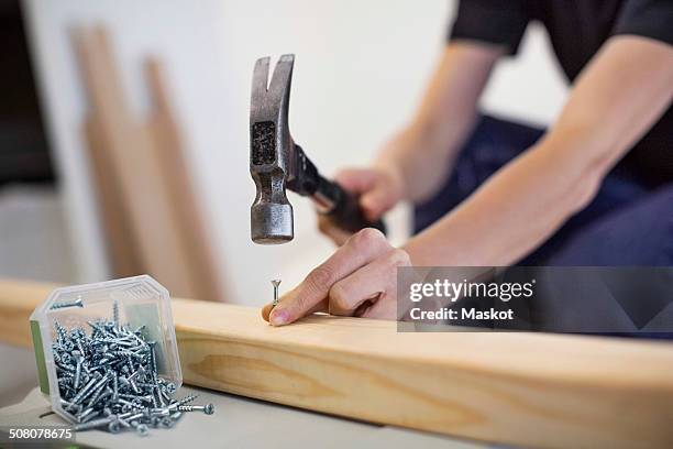 midsection of female carpenter hammering nail into wooden plank - hammer and nail fotografías e imágenes de stock