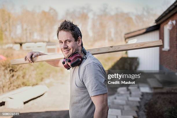 side view portrait of smiling carpenter carrying wooden plank at construction site - manual worker stock pictures, royalty-free photos & images