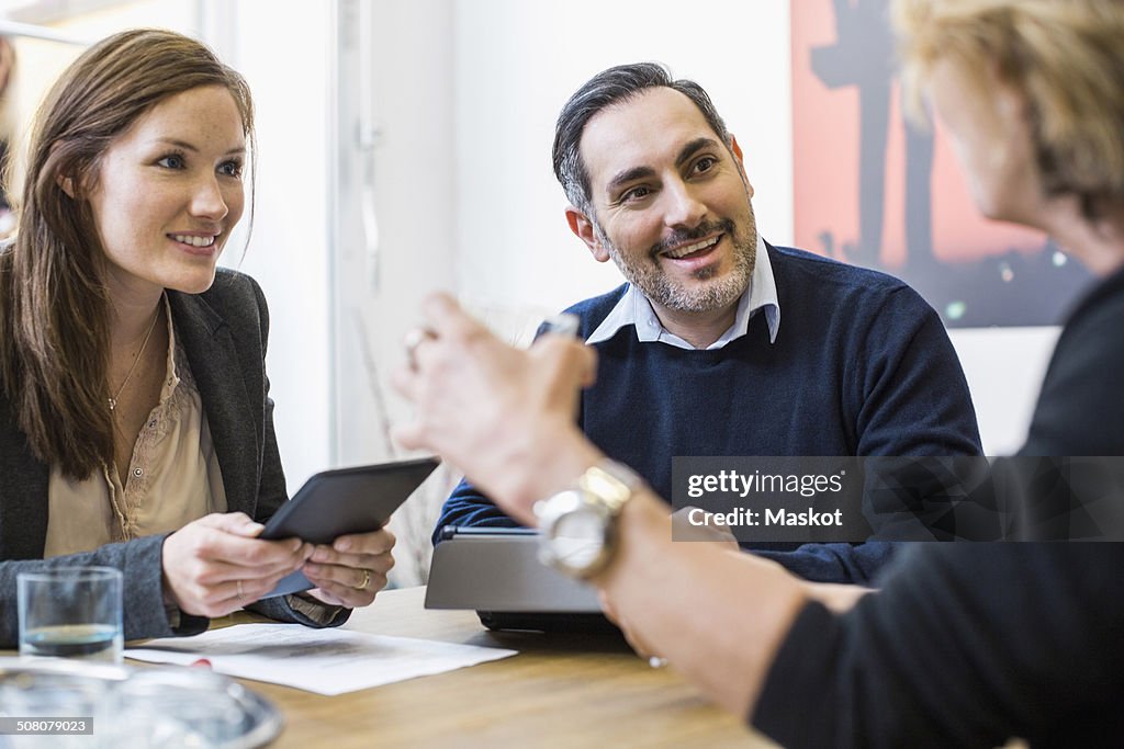 Smiling businesspeople with digital tablets discussing at desk in office