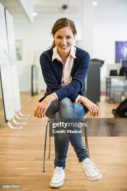 full length portrait of confident businesswoman sitting on chair in office - sitting in a chair stockfoto's en -beelden