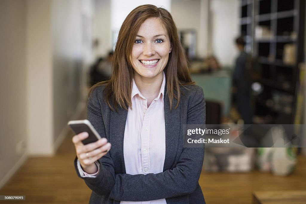 Portrait of smiling businesswoman holding mobile phone in office