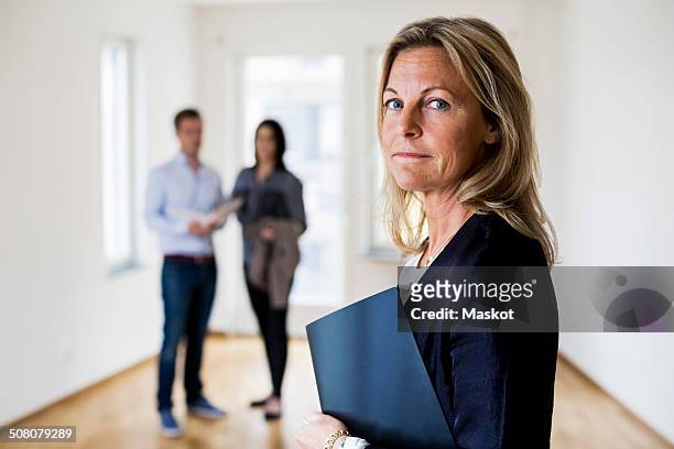 portrait of confident female real estate agent with couple standing in background at home - selling house stockfoto's en -beelden