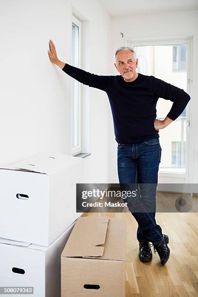 full length of mature man standing by moving boxes at home - leaning stock-fotos und bilder