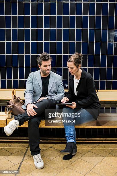 full length of business people discussing over digital tablet while sitting on bench at subway station - stockholm metro stock pictures, royalty-free photos & images