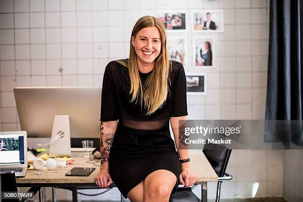 portrait of smiling young businesswoman leaning at table in new office - fashion designer stockfoto's en -beelden