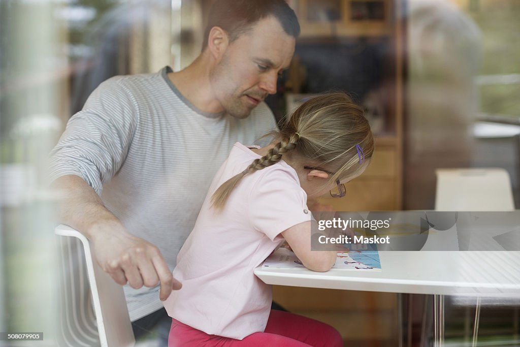 Father assisting handicapped girl in studies at table