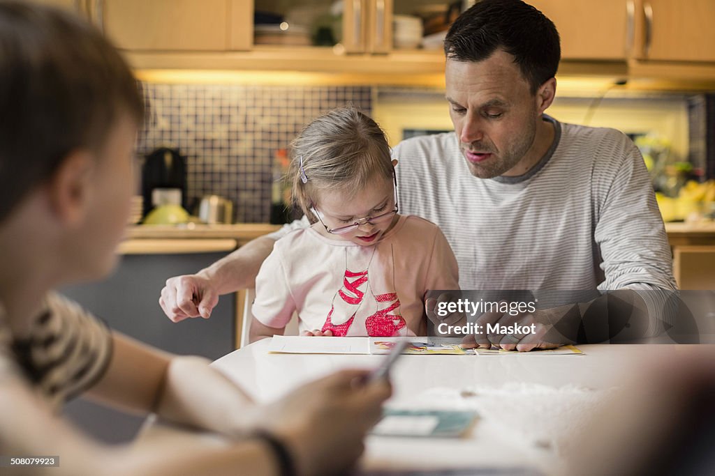 Father teaching daughter with son in foreground at home