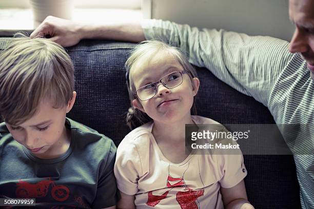 Girl with down syndrome looking at father by brother on sofa