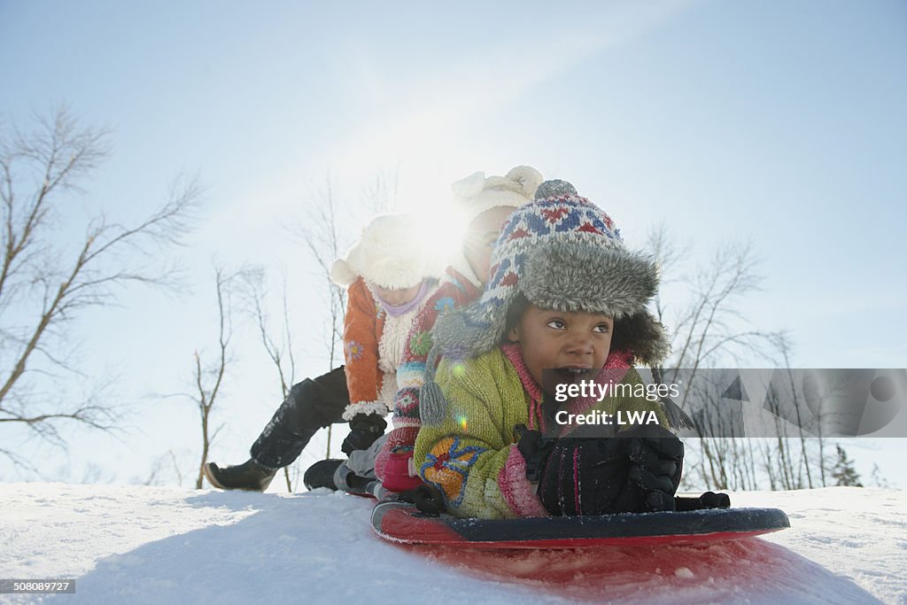 Young girl pushing sisters on sled