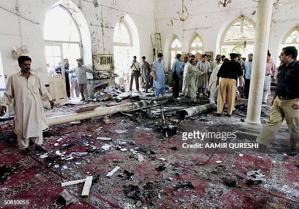 Pakistani worshippers and police officers walk through the wreckage inside a Shiite Muslim mosque after a a bomb ripped through during holy Friday...