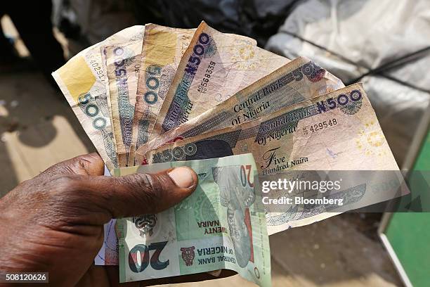 Trader holds 20 and 500 denomination naira banknotes at the Swali market in Yenagoa, Nigeria, on Thursday, Jan. 14, 2016. With his security forces...